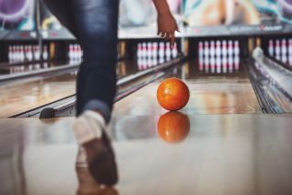 Ein Person steht auf einer Bowling-Bahn und bowlt
